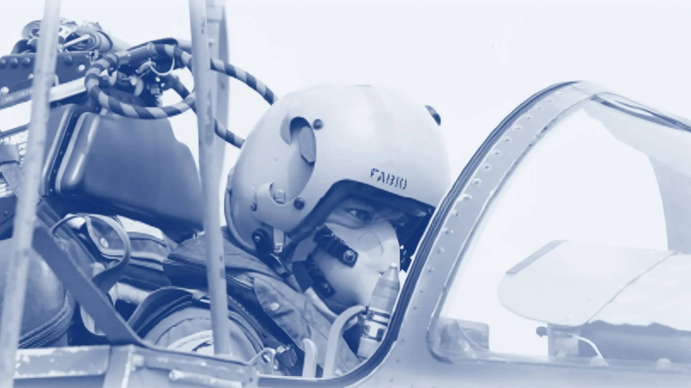 Fabio Masci in a fighter cockpit, in a flight helmet with his name and an oxygen mask, tinted blue