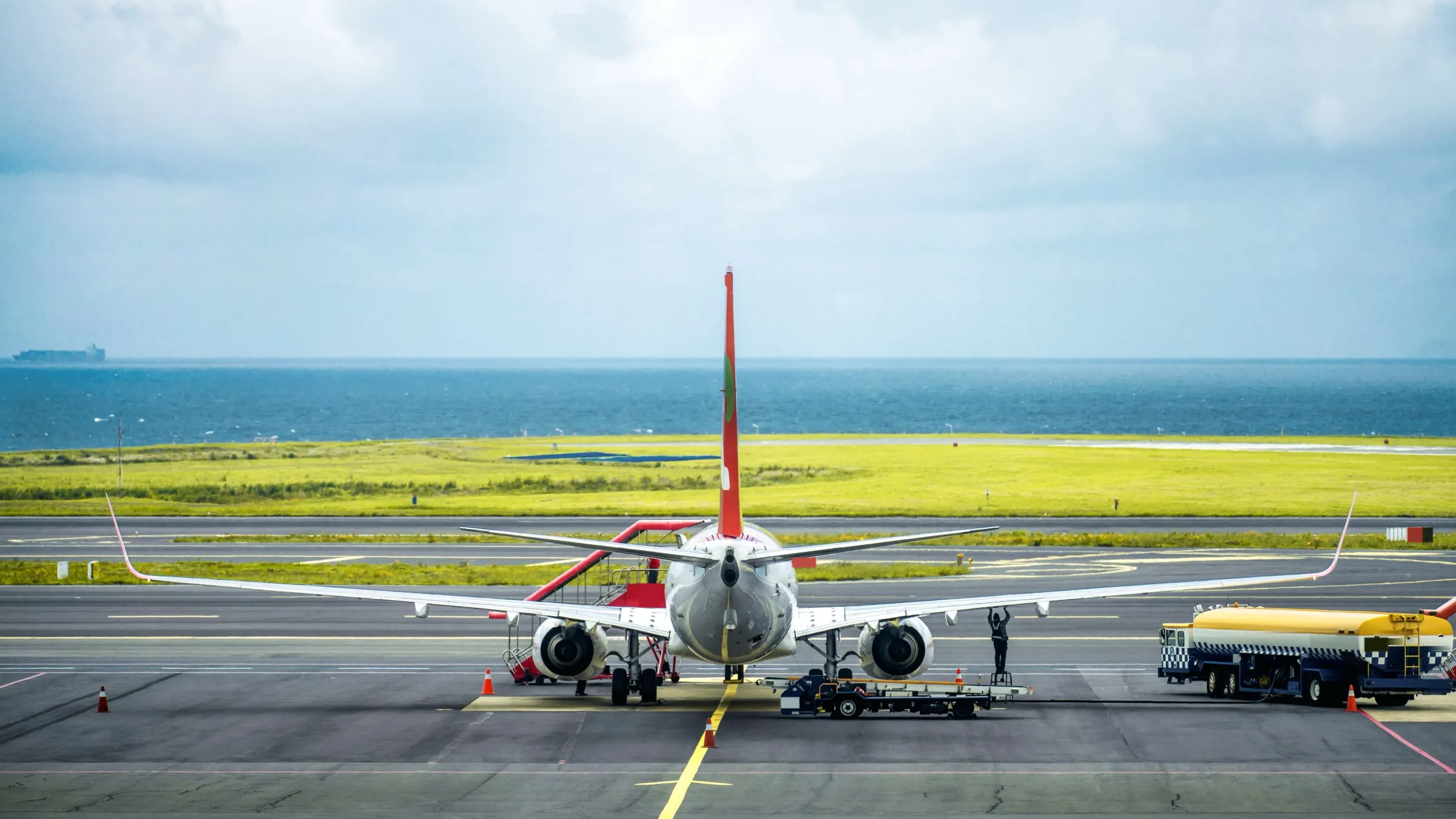An airliner parked on an airport apron, the runway and a strip of sea beyond, tinted blue